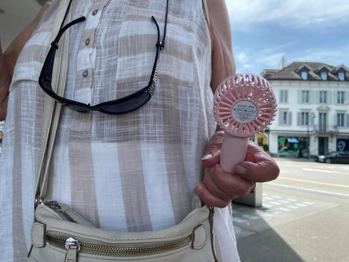 Eine Frau hält einen kleinen rosa Ventilator in der Hand.